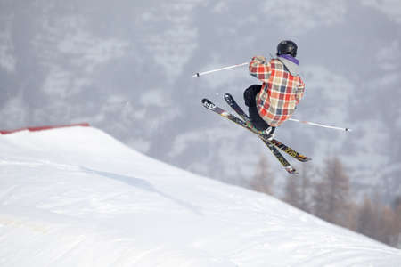 A free-ride ski jumper, with skis crossed against a mountains