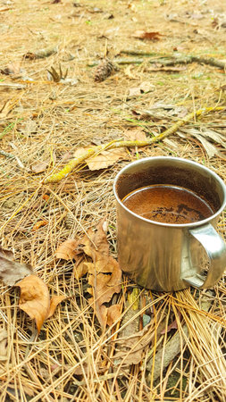Hot tea in a metal cup on the ground in the autumn forestの写真素材