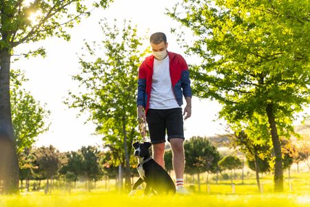 man wearing a protective mask is walking alone with a dog outdoors because of the corona virus pandemic covid-19の写真素材