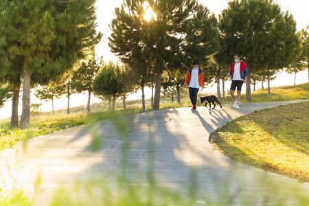 Young couple wearing a protective mask is walking alone with a dog outdoors because of the corona...