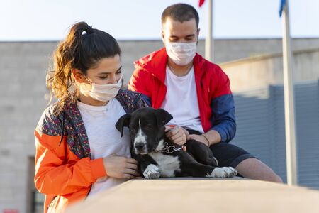 young couple wearing a protective mask is walking alone with a dog outdoors because of the corona virus pandemic covid-19の写真素材