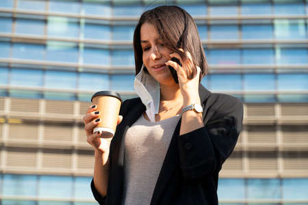 Woman taking her mask talks on the phone when she drinks coffeeの写真素材
