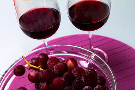 red wine in the wine glass, grape in the vase on the glass table