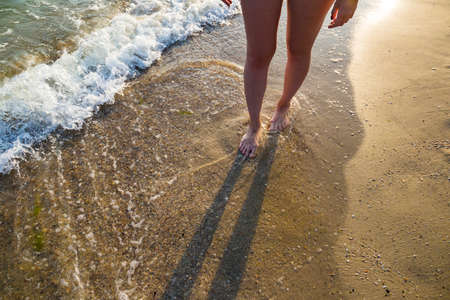 Girl with beautiful legs walks near the sea at sunsetの写真素材