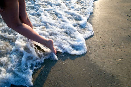 Girl with beautiful legs enters the sea at sunset の写真素材
