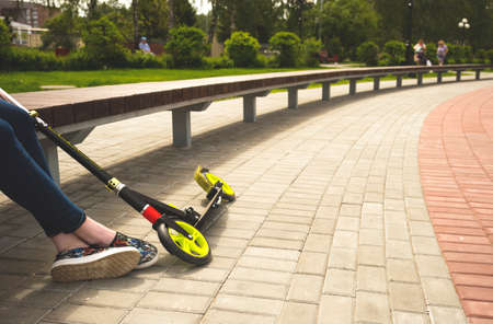 A girl with a kick scooter sits on a bench on the street. Copy spaceの写真素材