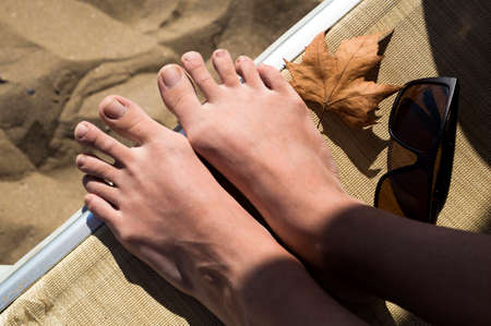 autumn beach: the first autumn leaf, girl legs, sunglasses near the seaの写真素材