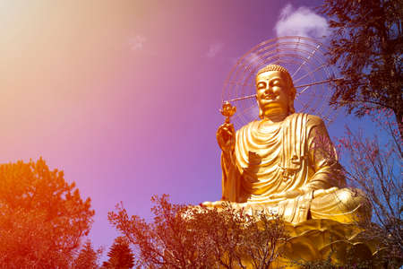 a large, majestic and beautiful figure of a seated golden buddha in Dalat, Vietnam on the sunset sky backgroundの写真素材