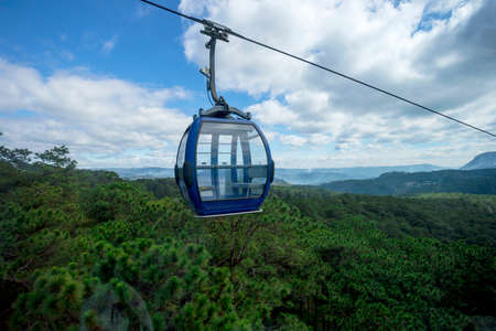 A scenic cable car with colorful cabs over mountains with green forests with blue cloudy sky on the backgroundの写真素材