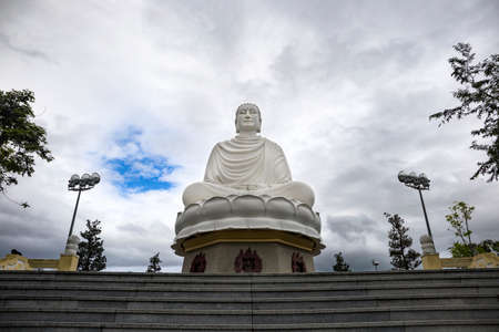 large statue of a white Buddha in lotus position near a Buddhist pagodaの写真素材