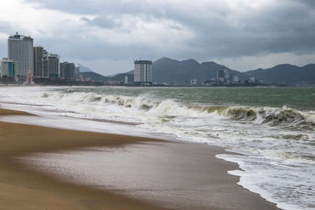 storm with big waves on the seashore with city and mountains on the backgroundの写真素材