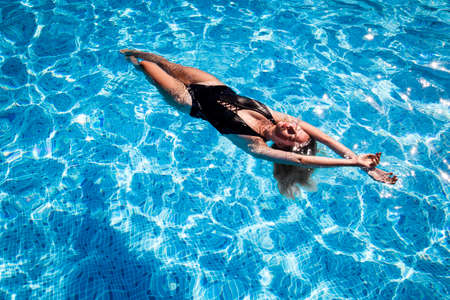 beautiful girl relaxes in the swimming pool in sunny day の写真素材