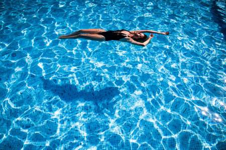beautiful girl relaxes in the swimming pool in sunny day の写真素材