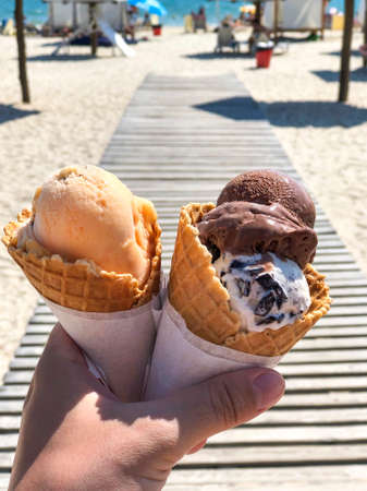 Fresh tasty bright ice cream in the hands with beautiful sea and sand beach in sunny day on the...