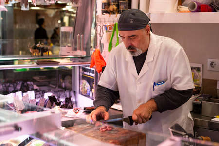 mature butcher cutting meat wuth the big special knife at the famous market at Barcelona, Catalonia, Spain 2019-04-30のeditorial素材