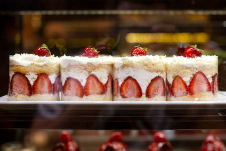 Delicious fresh strawberry cakes with cream on the confectionery showcase. Assortment of desserts in...