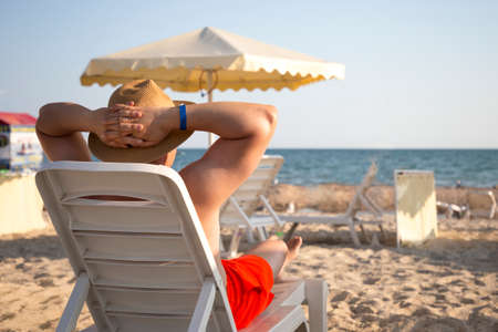 Young muscular attractive man in a hat lies on the lounger and looking at the sea or ocean. View...