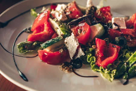 Popular greek vegetable salad with feta cheese and herbs. Plate with salad on the wooden table in the restaurant. Close up photo.の写真素材
