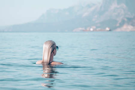 Girl swims in the turquoise sea. Back view of a girl with smooth wet blond hair.の写真素材