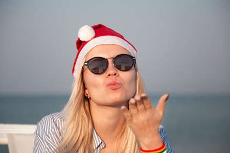 Girl in a red Christmas hat on the beach next to the sea. Holiday concept.の写真素材
