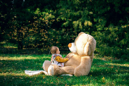 Little cute child is playing with a big bear on a green lawn.のeditorial素材