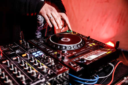DJ plays live set and mixing music on turntable console at stage in the night club. Disc Jokey Hands on a sound mixer station at club party. DJ mixer controller panel for playing music and partying.の写真素材