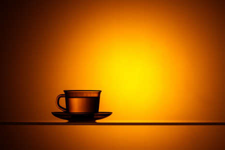 Cup and saucer with a transparent liquid on a bright orange background. Water or tea in the light.の写真素材