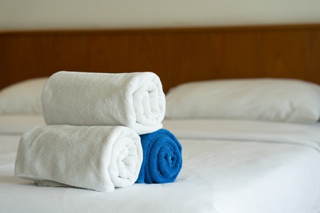 White and blue towels roll up on bed in hotel bedroomの写真素材