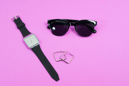 Concept travel on holiday. Sunglasses with black watch and earring on pink background.の写真素材