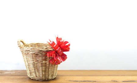 Wicker basket with red ribbon on wooden table and white background.の写真素材
