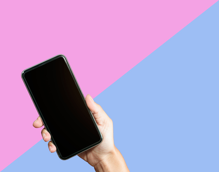 Hand holding mock up smart phone on pink and blue background.の写真素材