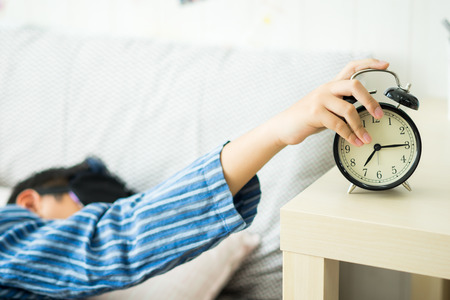 A kids waking up to an alarm clock in the bedroomの写真素材