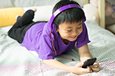 Kid listening to music on bed in bedroomの写真素材