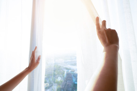 Hand woman is opening the curtain at the window in the morning.の写真素材