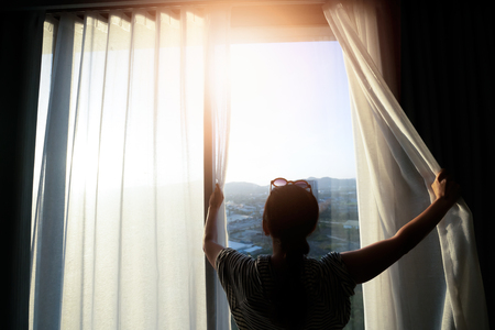 Beautiful woman is opening the curtain at the window in the morning.の写真素材