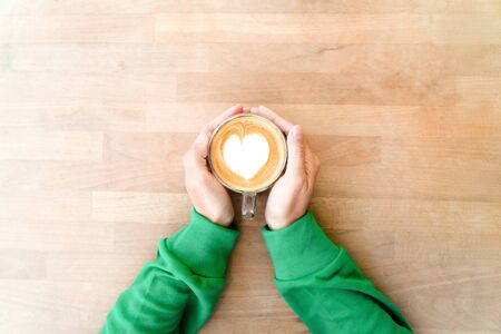 Hand holding hot coffee with heart milk froth