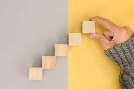 Woman hand arranging empty wood block and copy space on grey and yellow backgroundの写真素材