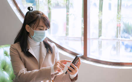 Business woman wearing surgical mask and using smartphone for work, social mediaの写真素材
