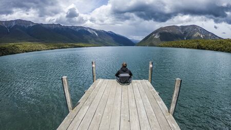 Man sitting on wooden pier on a lake enjoying panorama