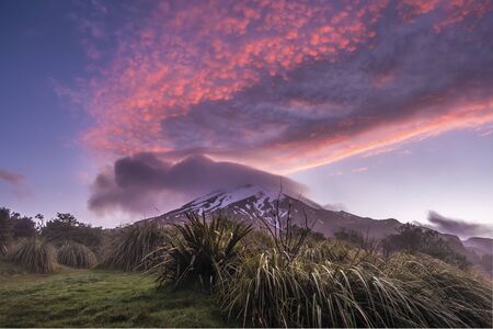 Mountain in a clouds during colorful red sunset and green grass in frontの写真素材