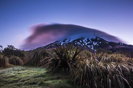 Mountain in a clouds during colorful purple sunset and green grass in front