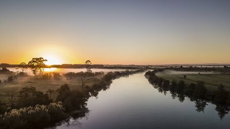 Aerial view on a calm river reflection during orange sunrise