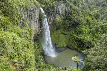 Steep cliff with waterfall and pond in the middle of green forest