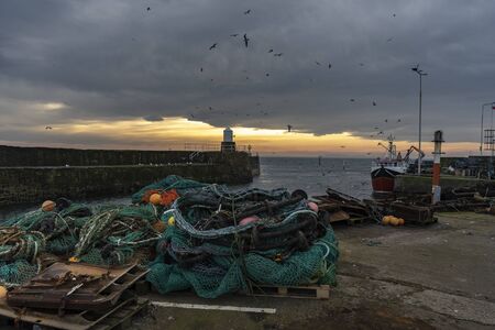 Historical harbor with an old traditional fishing nets boat and lighthouse during cloudy sunset