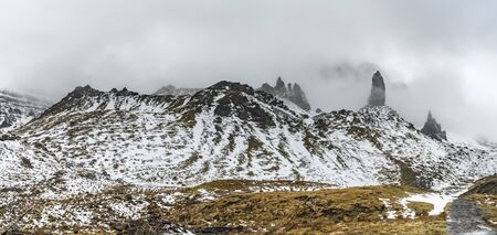 High snowy rocks hidden in a mist with meadow full of grass