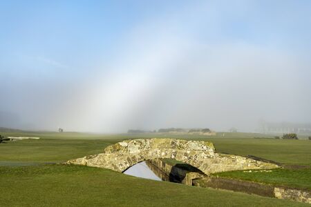 Old stone bridge in a green fields with white vapor in a skyの写真素材