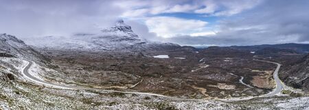 Panoramic view with snowy mountain road and cloudy sky