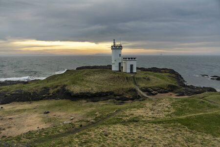 Lighthouse on the green cliffs with a cloudy sunset on a backgroundの写真素材
