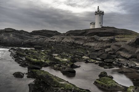 Lighthouse on the sea shore rocks during cloudy dayの写真素材