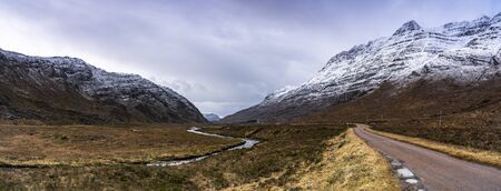 Snowy mountains with river and large meadows of grass in a winterの写真素材